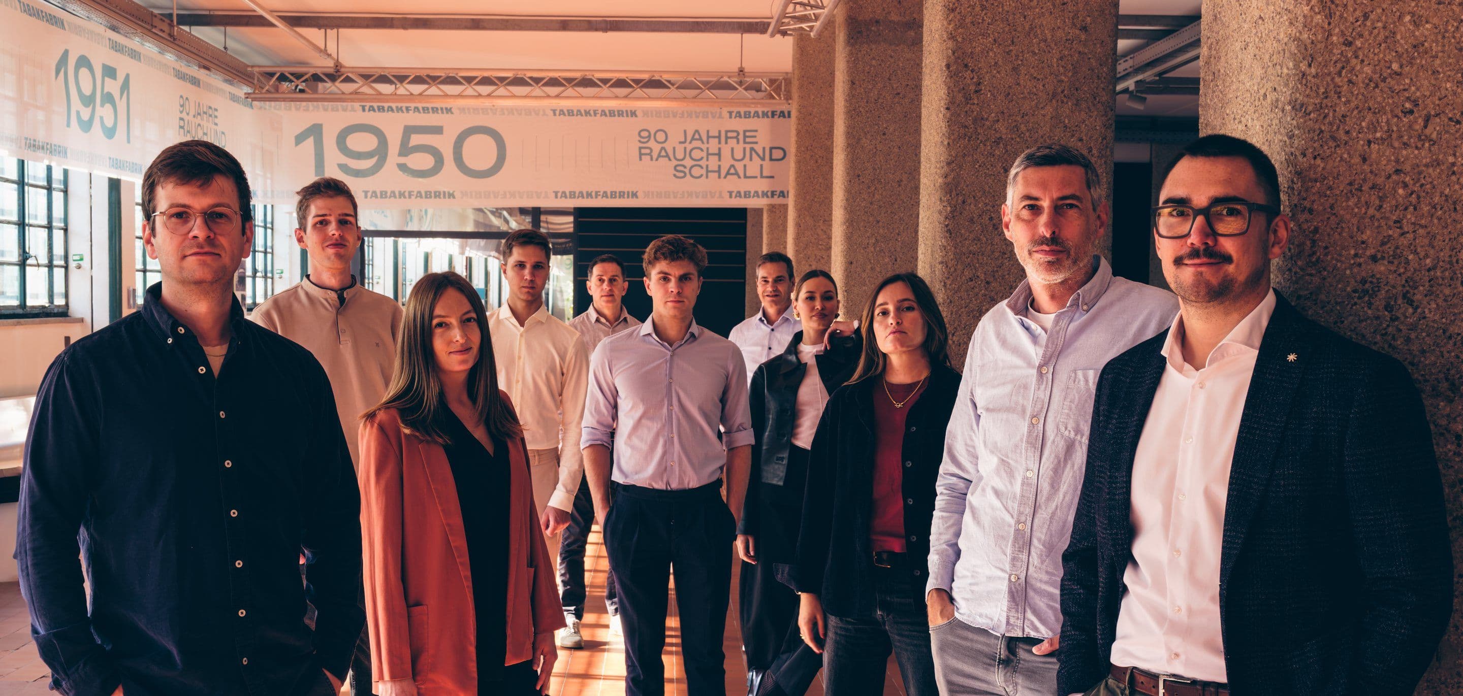 Das Team von Minotera steht gestaffelt in der Säulenhalle der Tabakfabrik Linz