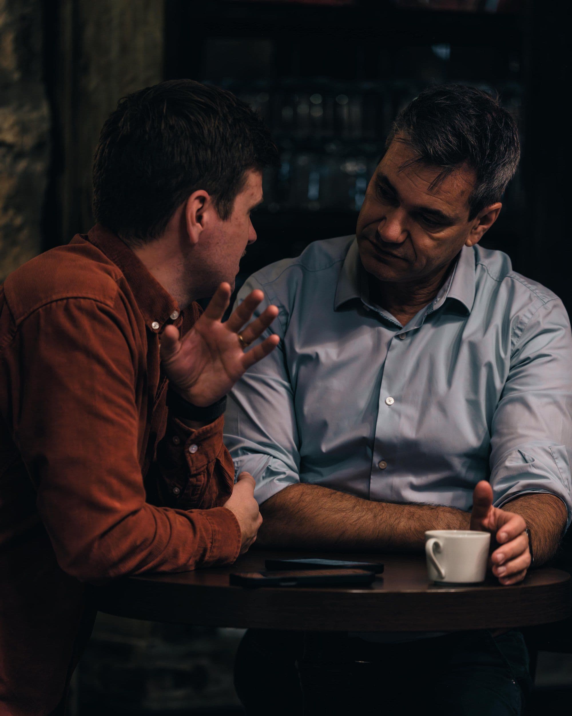Julian Kranner und Wolfgang Auer im Gespräch an einem Tisch, eine Kaffeetasse zwischen ihnen